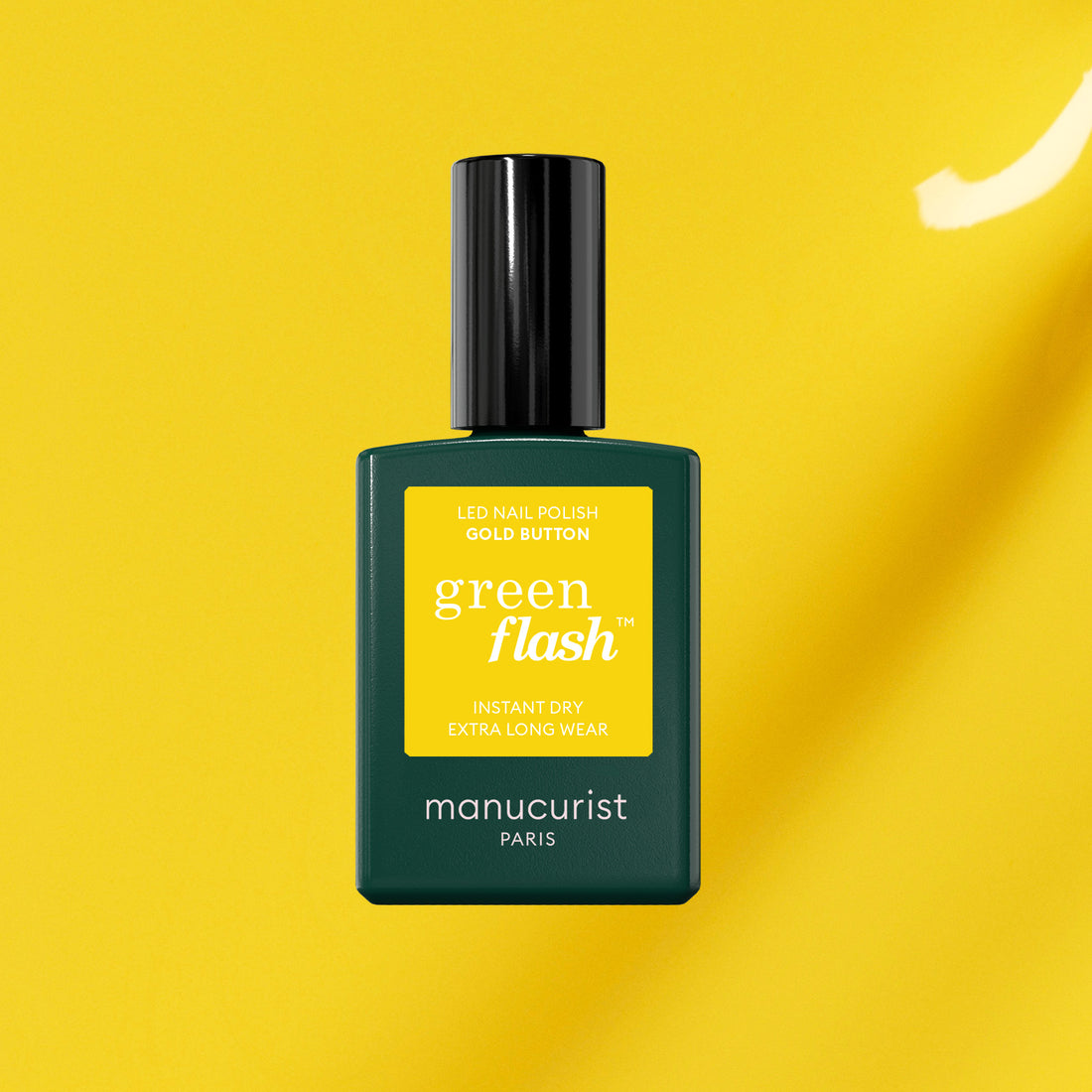 Un flacon de vernis gel Manucurist Gold Button avec un bouchon noir et une étiquette verte, présenté sur un fond jaune vif.