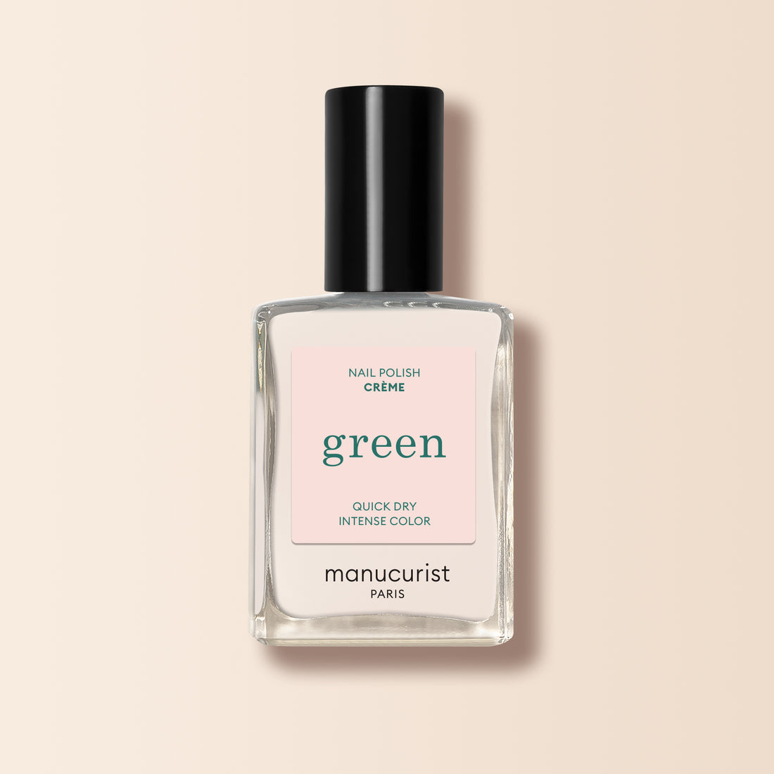 Un flacon en verre transparent de vernis à ongles Manucurist Crème, avec un bouchon noir et une étiquette rose clair, repose sur un fond beige.