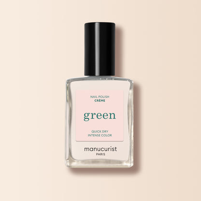 A clear glass bottle of Manucurist Crème nail polish with a black cap and light pink label rests on a beige background.