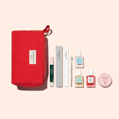 A red Manucurist pouch labeled "Paris" displays the Healthy Glow Duo, featuring a green-tipped serum pen, two nail files, a cuticle pusher, three bottles of nail treatment or polish, and balm on a light backdrop.