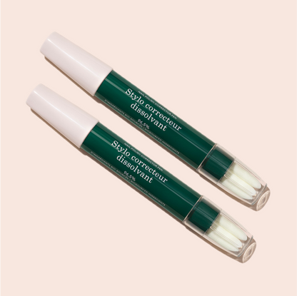 Two green and white Manucurist-test [Test jauge] Nail Polish Corrector Pens with clear caps, labeled "Stylo correcteur dissolvant," are positioned diagonally on a light beige background—ideal for precise gel polish touch-ups.