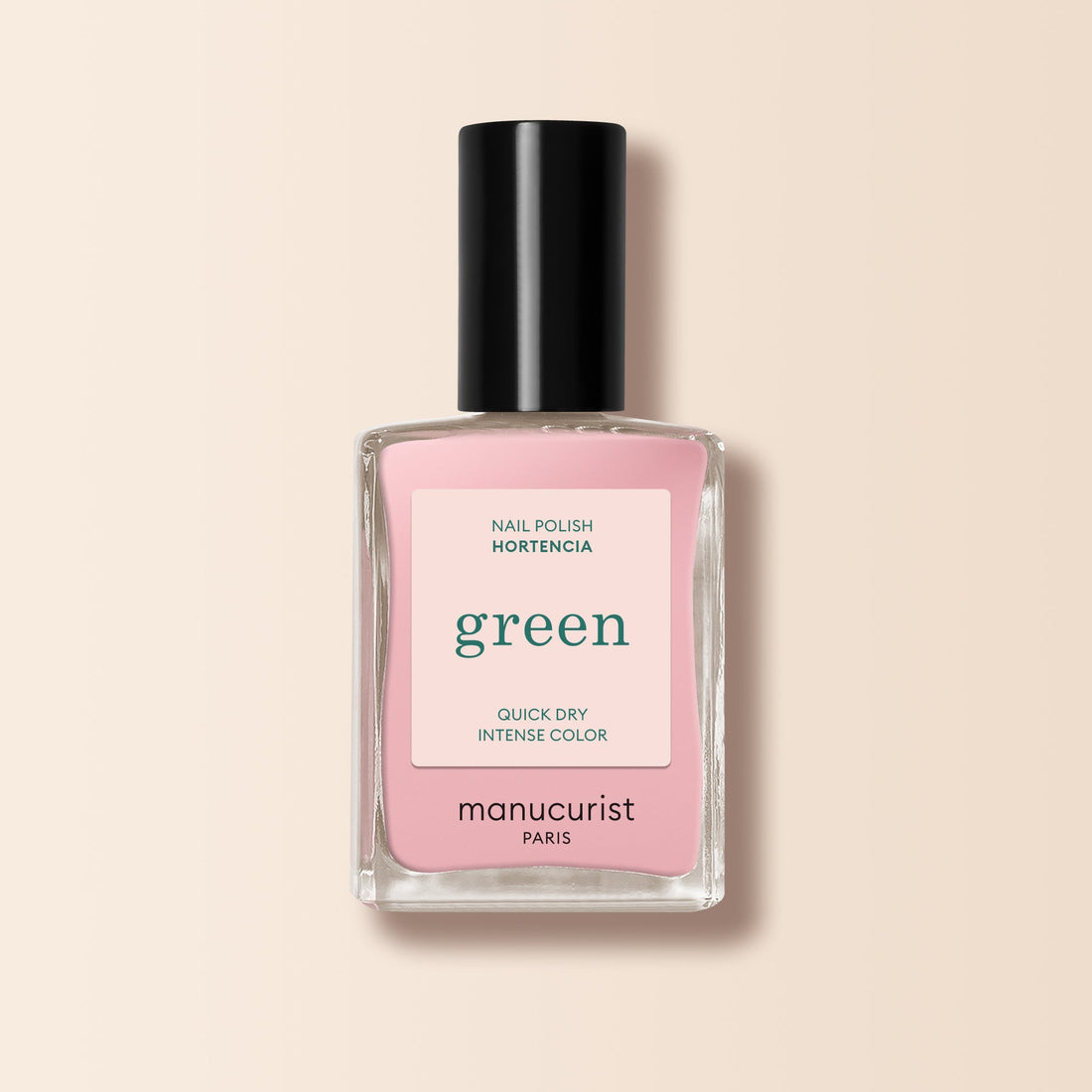Un flacon de vernis à ongles Manucurist dans la teinte Hortencia est posé sur un fond beige pâle. L’étiquette indique : green, séchage rapide, couleur intense. Le bouchon est noir.