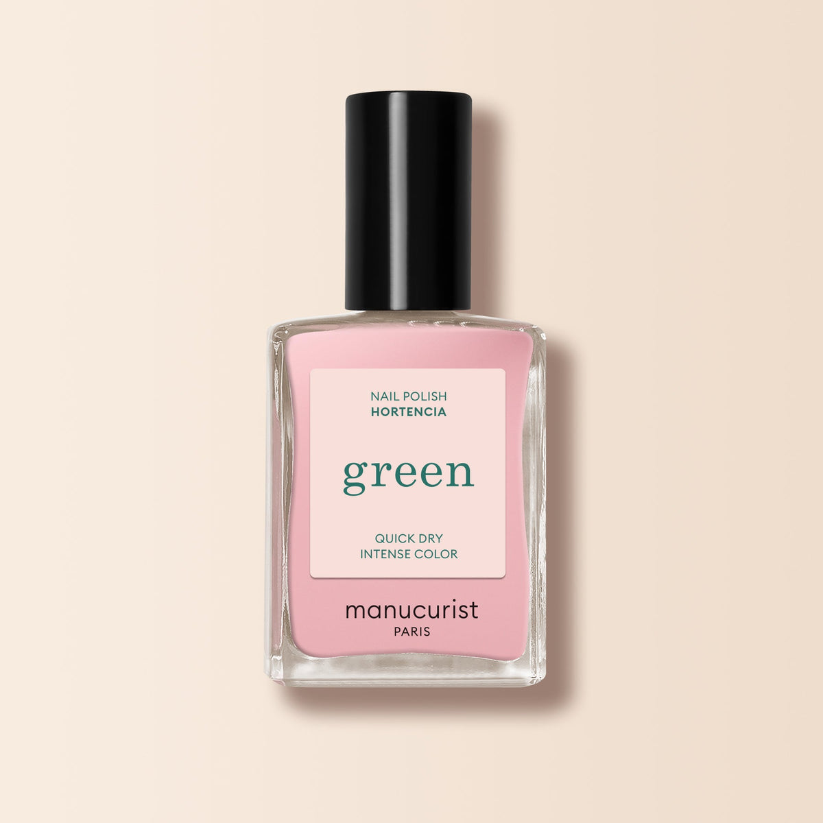 Un flacon de vernis à ongles Manucurist dans la teinte Hortencia est posé sur un fond beige pâle. L’étiquette indique : green, séchage rapide, couleur intense. Le bouchon est noir.