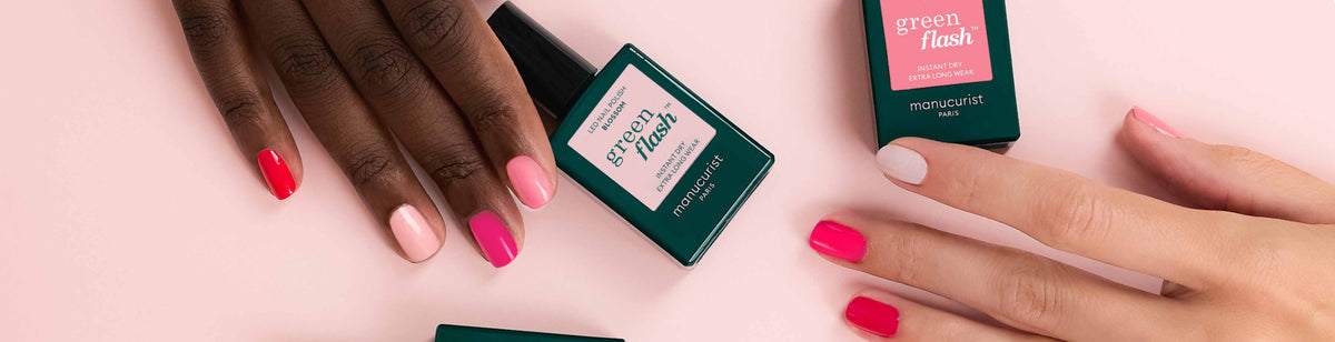 Two hands with manicured nails in shades of pink and white are displayed alongside bottles of Green Flash nail polish on a light pink surface.