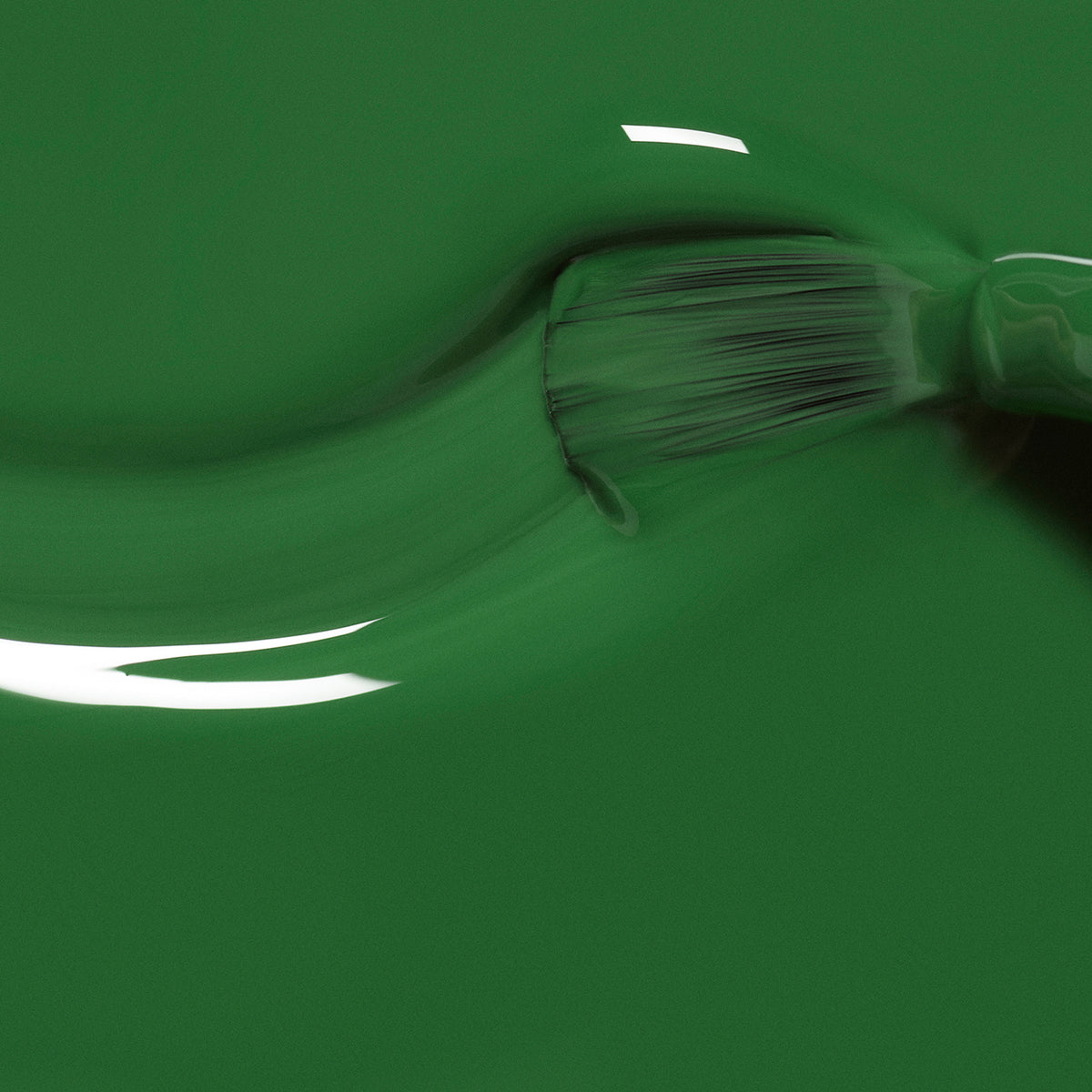 A close-up of a paintbrush applying Manucurist Jade, a glossy mineral green polish, across a smooth surface, with visible brush bristles and shiny reflections on the wet finish.