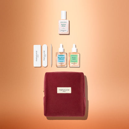The Manucurist Active™ Discovery Gift Set is beautifully displayed on a peach background and features a red velvet pouch, nail files, cuticle pusher, two bottles of nail care oil, and a bottle of nail serum—all perfectly arranged. This set makes an ideal holiday gift for anyone who loves a relaxing manicure routine and gorgeous nails.