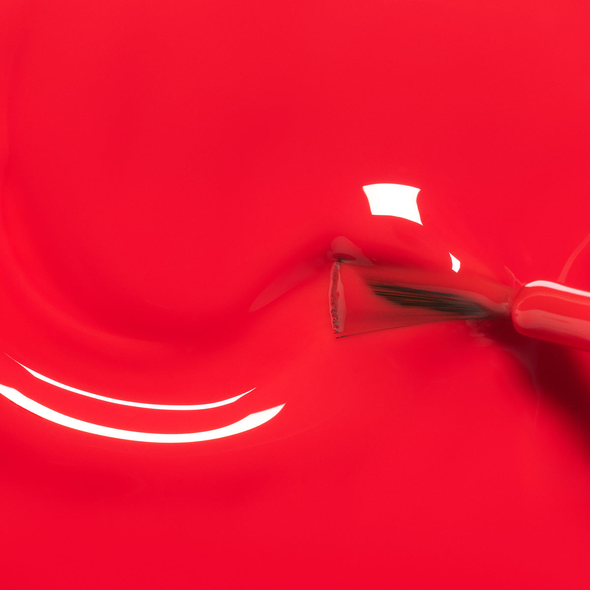A close-up of a Manucurist Lucette the Warbler nail polish brush spreading bright red kids&