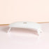 La lampe Manucurist Green Flash™ 24W — une lampe LED blanche, compacte et incurvée à quatre pieds — est posée sur une surface rose brillante, idéale pour les manucures au vernis gel Green Flash, sur un fond beige et rose.