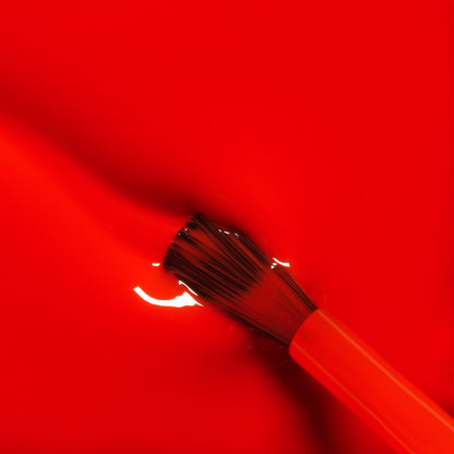 A close-up of a paintbrush with orange bristles dipped in Manucurist&