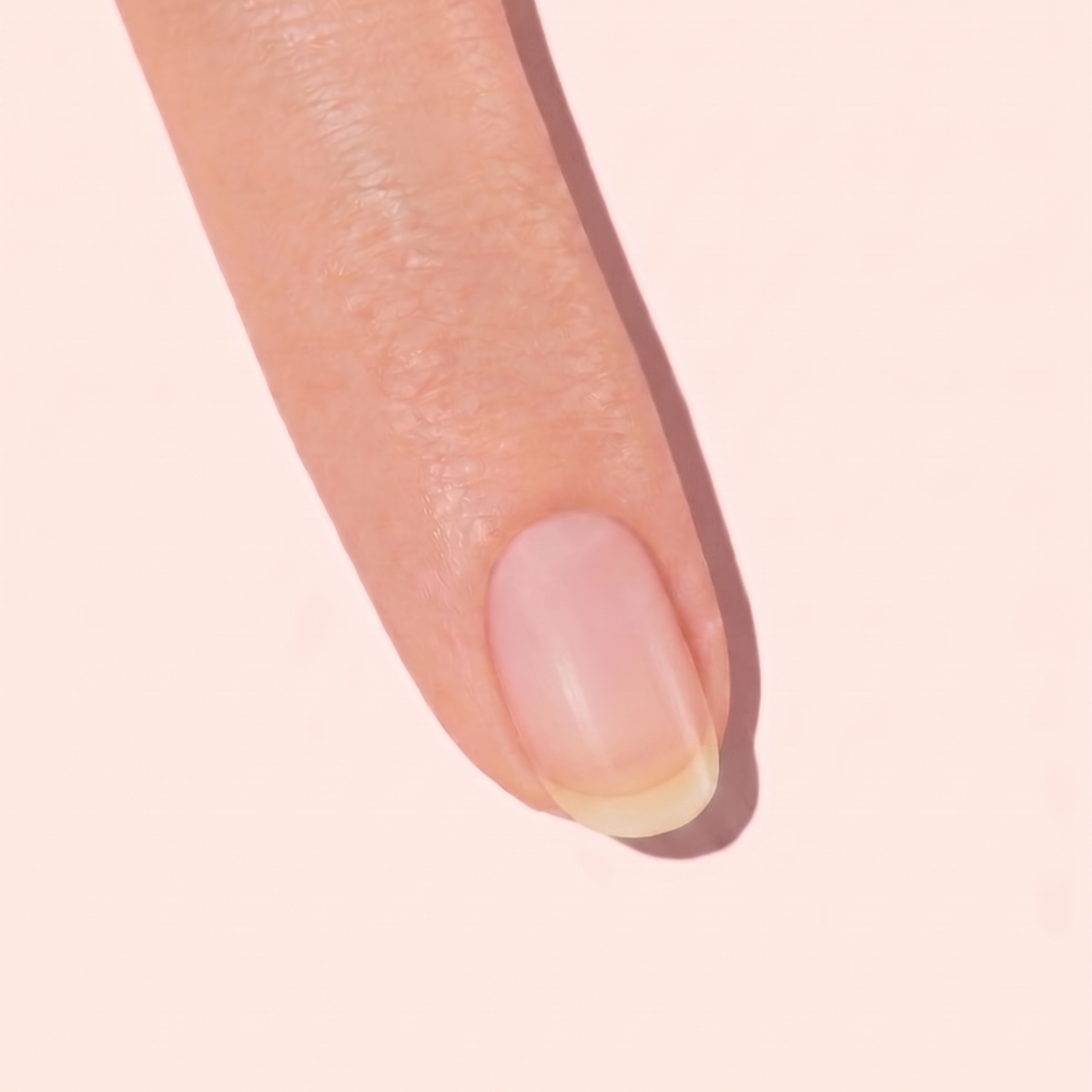 A close-up of a persons index finger with a natural, unpolished fingernail against a light pink background.