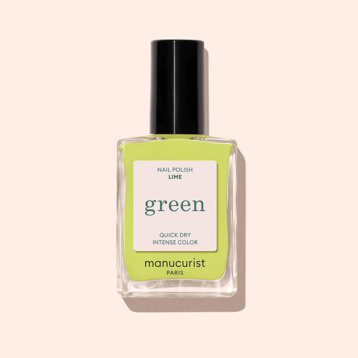A clear glass bottle of bright anise green nail polish called Lime by Manucurist, with a black cap, is placed on a light beige background.