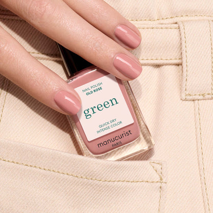 A hand with neatly manicured nails painted in Old Rose by Manucurist holds the bottle of nail polish against the pocket of beige pants.