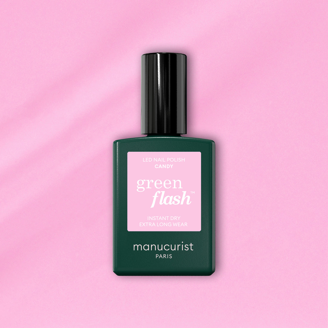 A bottle of Manucurist Candy Green Flash LED nail polish, with a pink label and dark green body, sits on a light pink background—ideal for those who love cool-toned LED manicures.