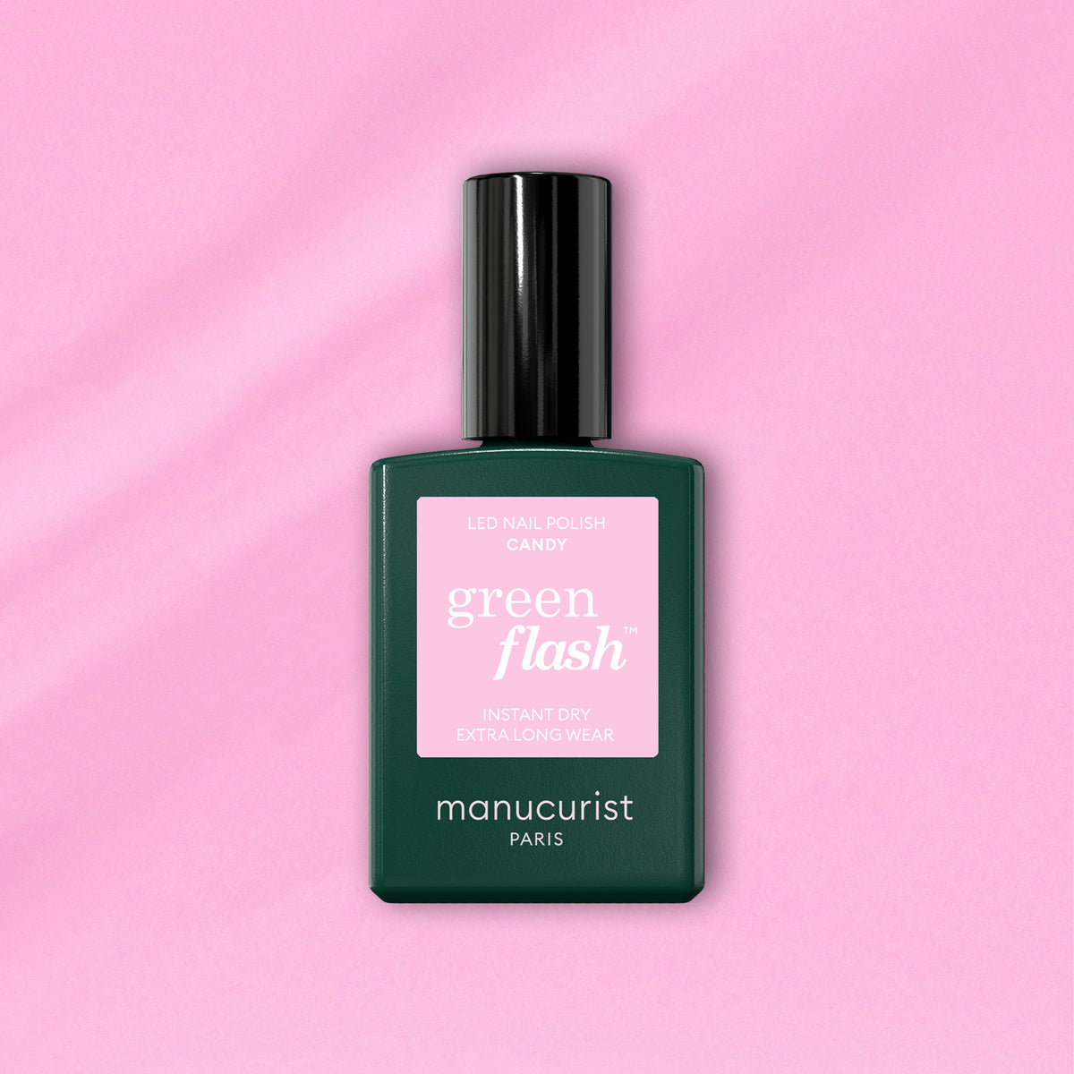 A bottle of Manucurist Candy Green Flash LED nail polish, with a pink label and dark green body, sits on a light pink background—ideal for those who love cool-toned LED manicures.