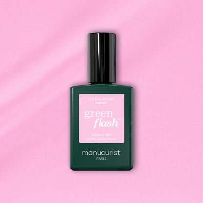 A bottle of Manucurist Candy Green Flash LED nail polish, with a pink label and dark green body, sits on a light pink background—ideal for those who love cool-toned LED manicures.