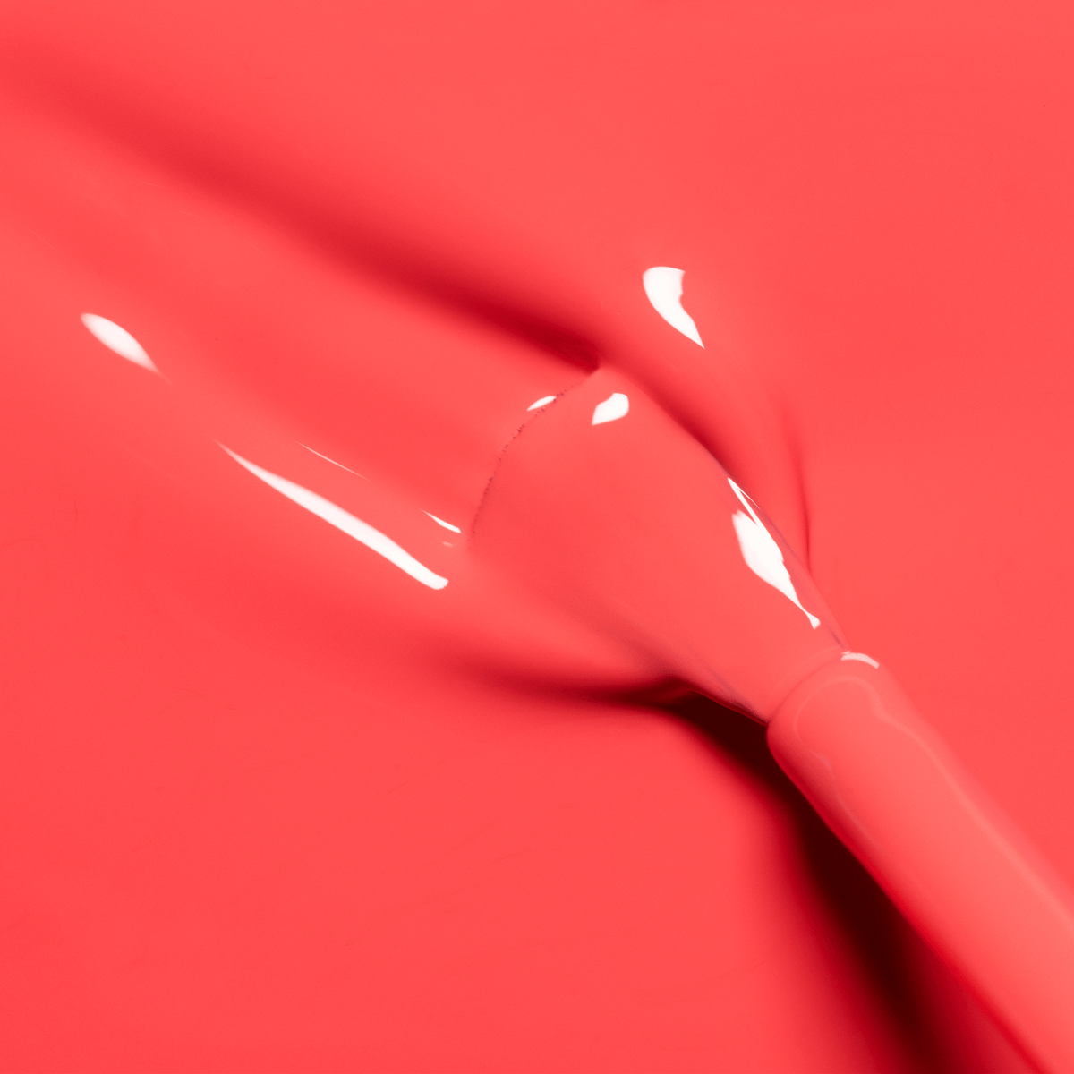 Gros plan sur un coup de pinceau de la teinte Pulp de Manucurist, un vernis pamplemousse vif et brillant, avec le pinceau partiellement visible et des traînées humides soulignant sa texture éclatante.