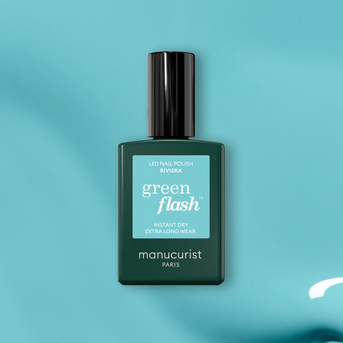A green bottle of Manucurist Riviera gel polish rests on a teal surface, displaying its Instant Dry and Extra Long Wear features.