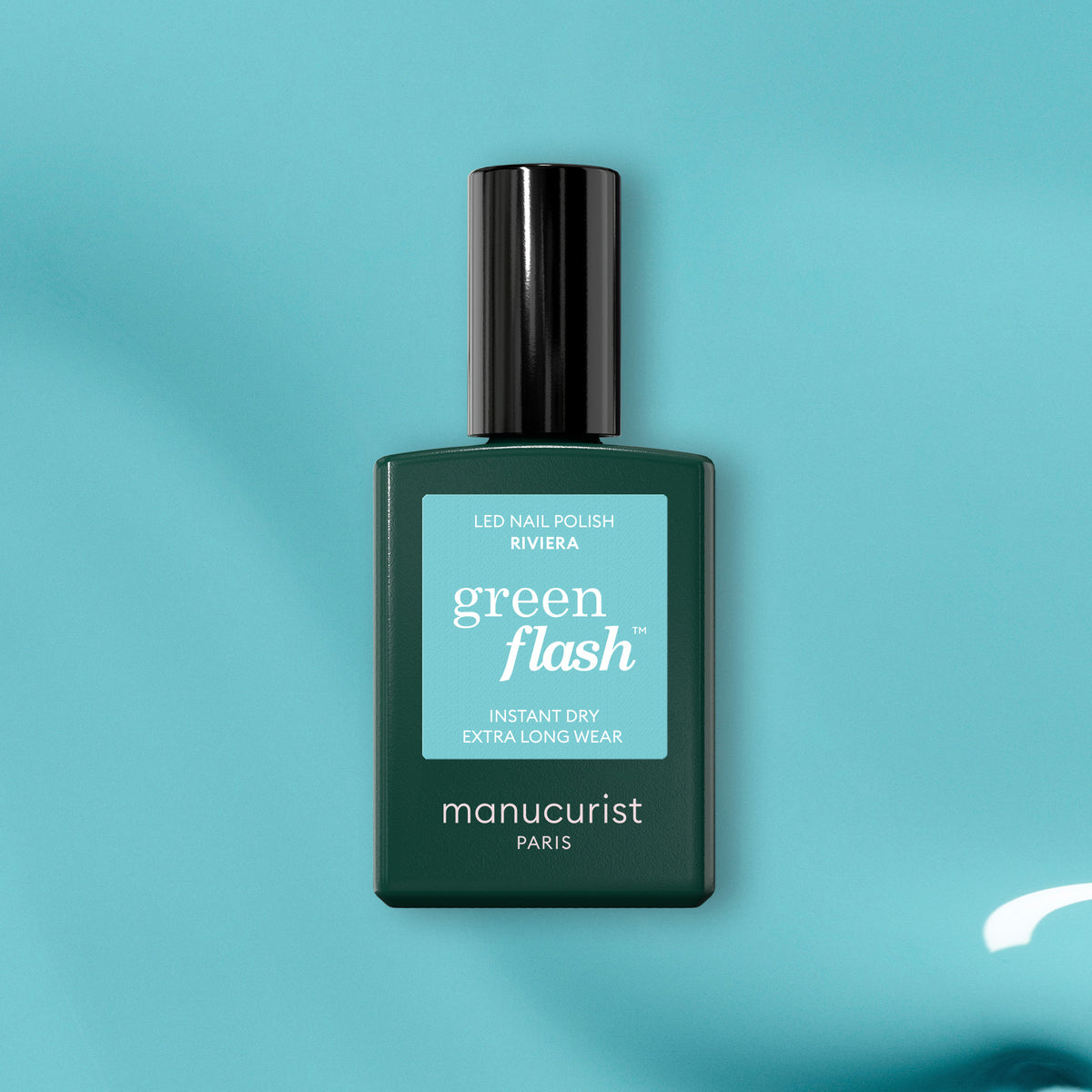 A green bottle of Manucurist Riviera gel polish rests on a teal surface, displaying its Instant Dry and Extra Long Wear features.