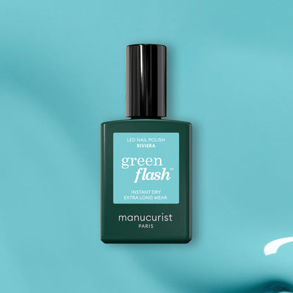 A green bottle of Manucurist Riviera gel polish rests on a teal surface, displaying its Instant Dry and Extra Long Wear features.
