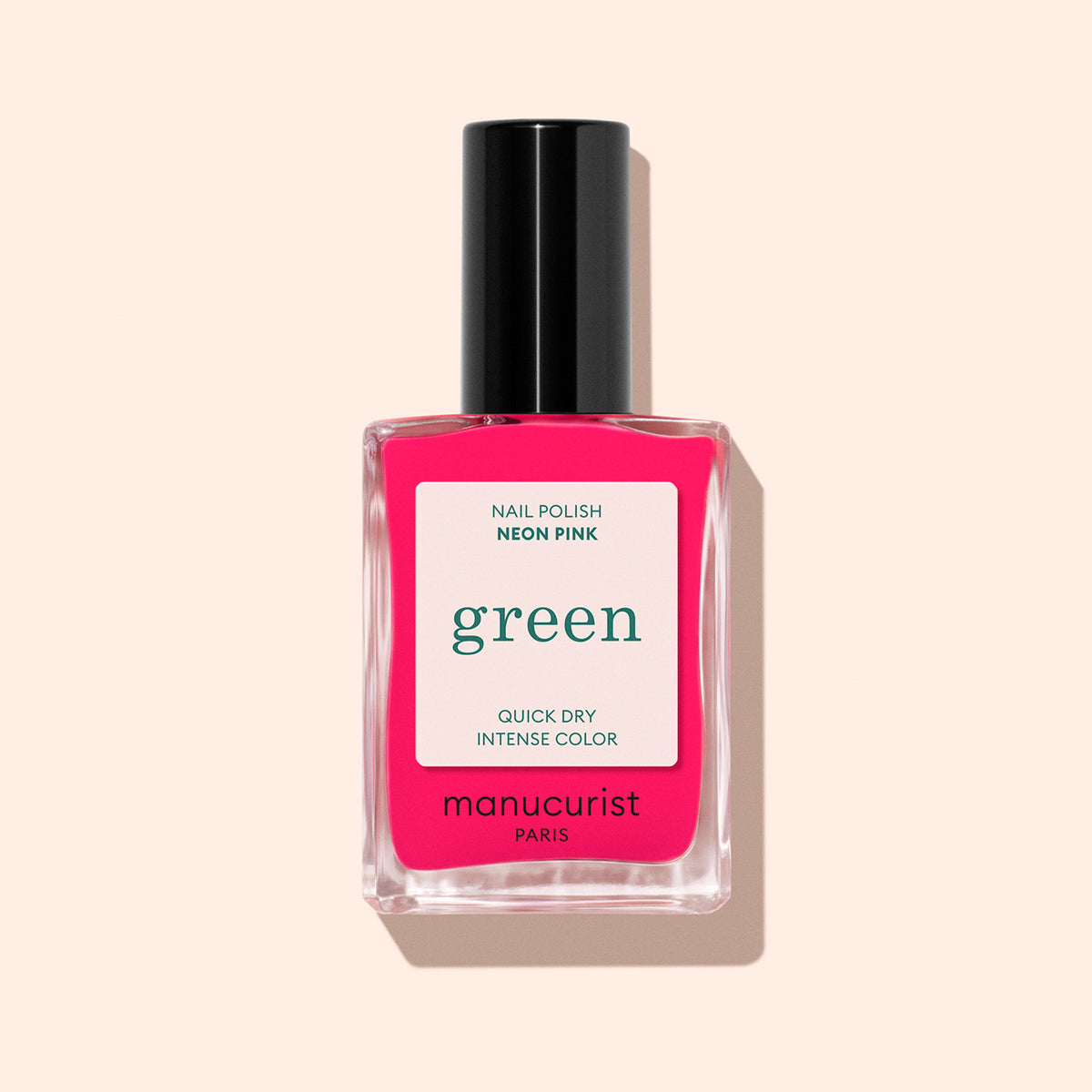 A bottle of Manucurist Neon Pink nail polish with a semi-matte finish and black cap, labeled green and quick dry intense color, sits against a pale peach background—ideal for vibrant summer nails.
