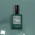 Un flacon de vernis à ongles LED Green Flash Sage de Manucurist se tient debout sur une surface vert sauge, avec un bouchon noir brillant et une étiquette minimaliste qui met en valeur sa douce teinte verte.