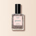 A clear bottle of Manucurist Quartz nail polish with a black cap, showcasing a shimmery light rose gold hue labeled “green” and “quick dry intense color” on a soft beige background.