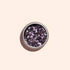 A small round container of Manucurist Lilac Biodegradable Glitter, featuring chunky, reflective mauve particles for nail art, sits on a light beige background and casts a soft shadow.