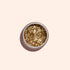 A round tin of Manucurist Gold Biodegradable Glitter rests on a light beige background with a soft shadow—ideal for dazzling nail art or pairing with your favorite gel polish.