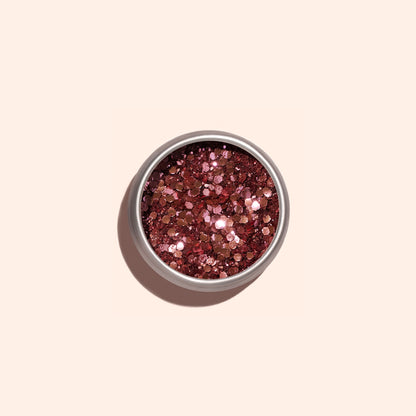 A small round container of Manucurist Pink Quartz Biodegradable Glitter, filled with shiny, chunky rose gold pieces, sits on a light beige background—perfect for adding eco-friendly sparkle to your nail art.