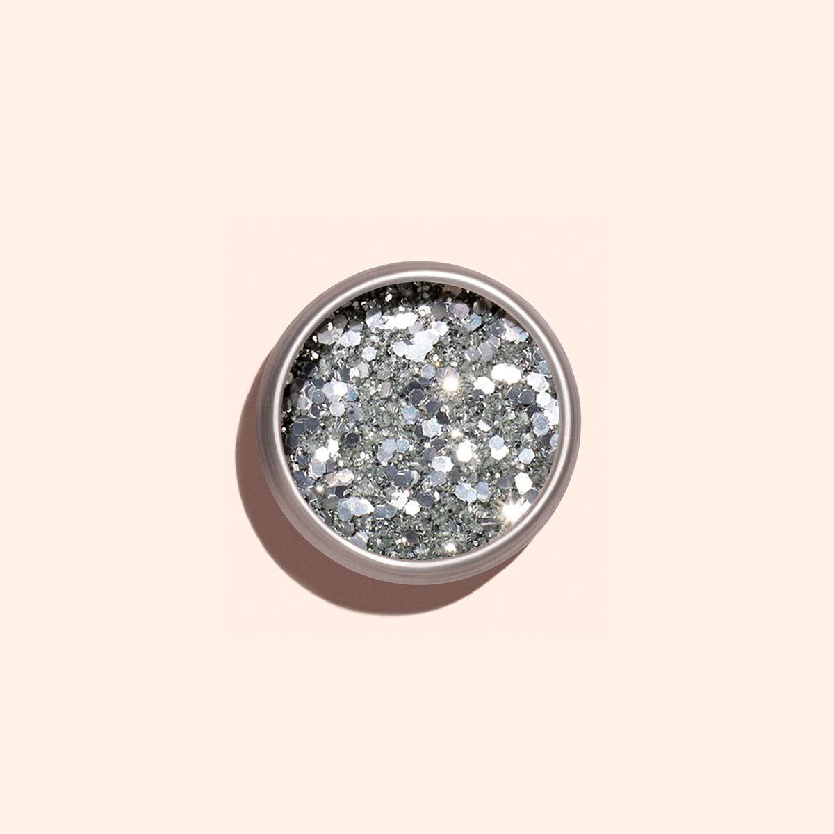 A round container of Manucurist Silver Biodegradable Glitter, designed for nail art, rests on a light beige background with a soft shadow cast to the left.
