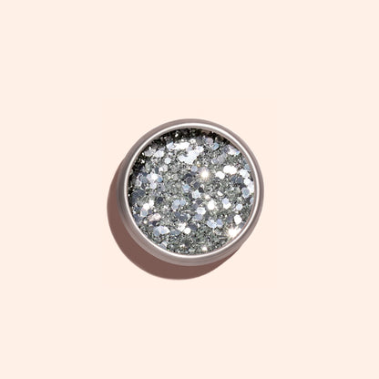 A round container of Manucurist Silver Biodegradable Glitter, designed for nail art, rests on a light beige background with a soft shadow cast to the left.