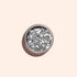 A round container of Manucurist Silver Biodegradable Glitter, designed for nail art, rests on a light beige background with a soft shadow cast to the left.