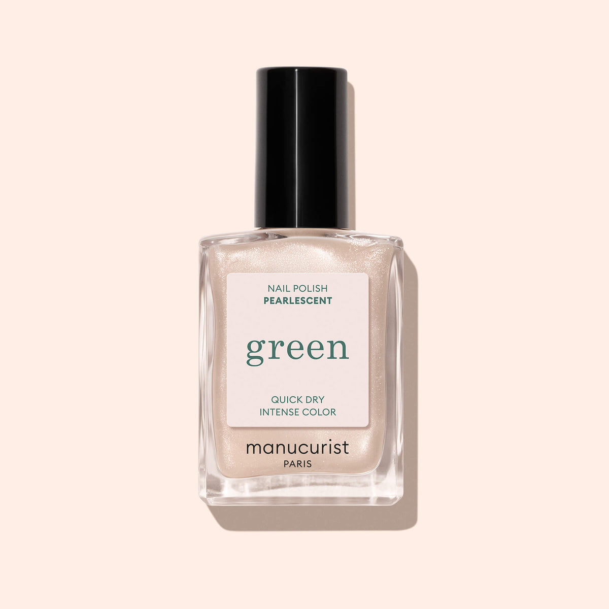 A bottle of Manucurist Pearlescent polish, a pearlescent beige shade with pink undertones, labeled green, sits in a clear rectangular glass bottle with a black cap against a light beige background.