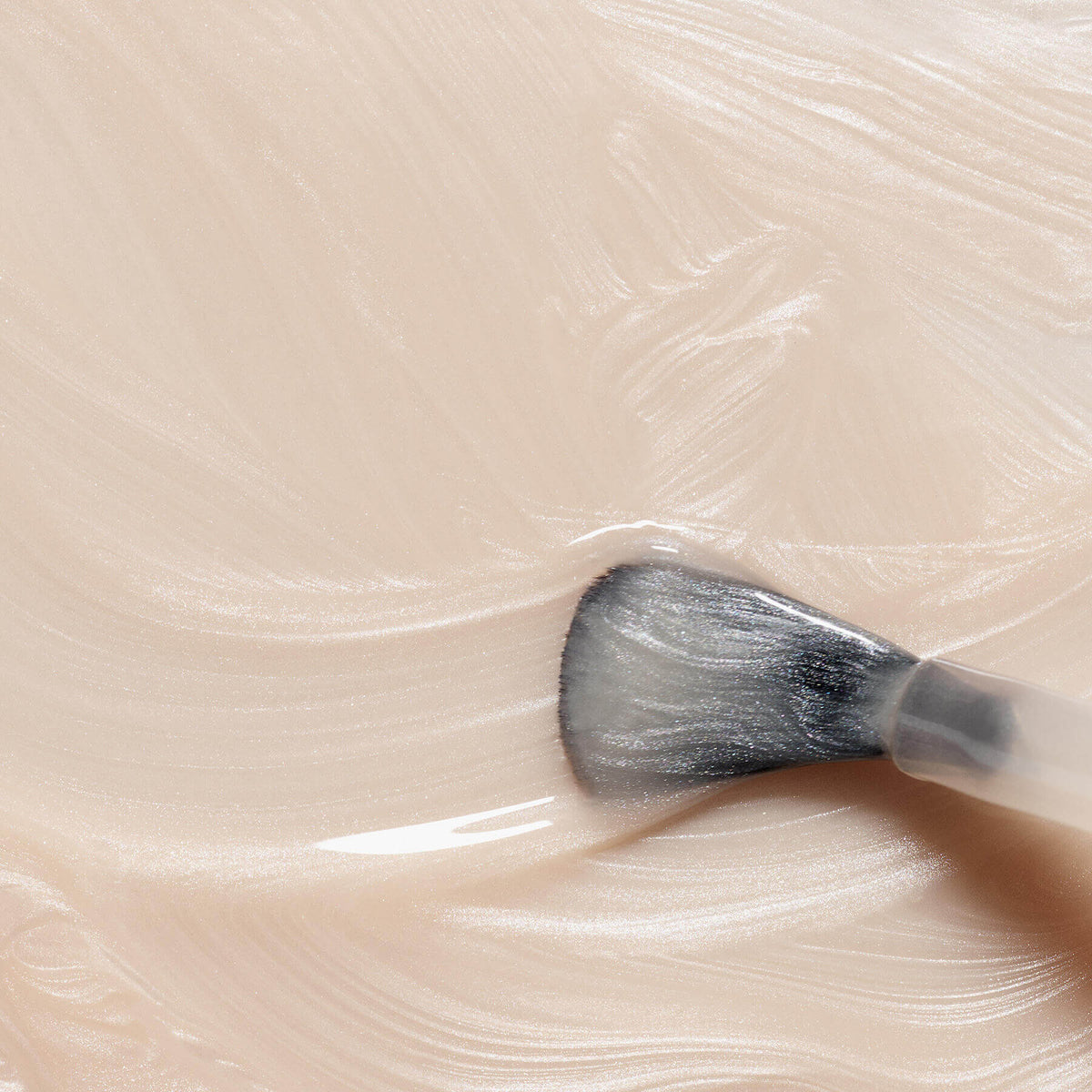 Gros plan sur un pinceau de maquillage estompant Pearlescent de Manucurist, un cosmétique beige clair crémeux aux sous-tons roses et à la texture lisse et brillante.