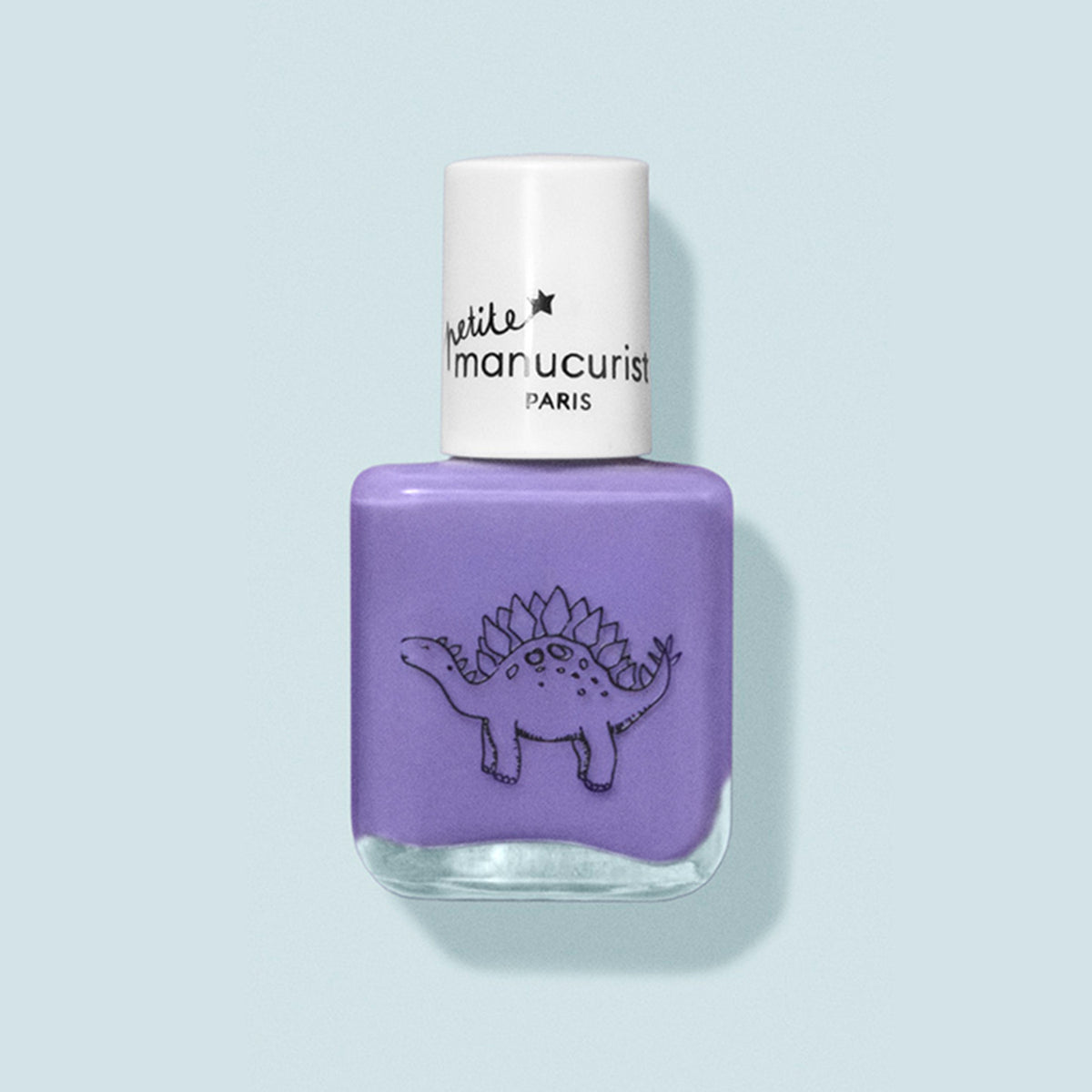 Un flacon de vernis à ongles violet pour enfants nommé Hector the Stegosaurus de Manucurist, avec un bouchon blanc. Il présente un dessin de dinosaure au trait noir et l’étiquette « petite Manucurist PARIS ». Fabriqué à partir d’ingrédients naturels. Le fond est bleu pâle.