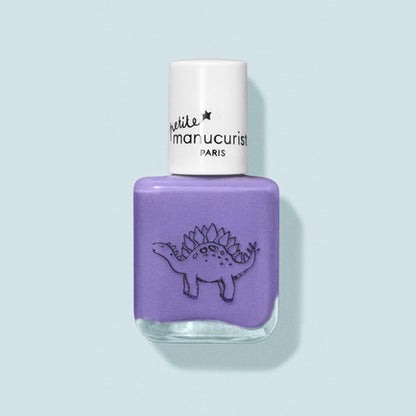Un flacon de vernis à ongles violet pour enfants nommé Hector the Stegosaurus de Manucurist, avec un bouchon blanc. Il présente un dessin de dinosaure au trait noir et l’étiquette « petite Manucurist PARIS ». Fabriqué à partir d’ingrédients naturels. Le fond est bleu pâle.