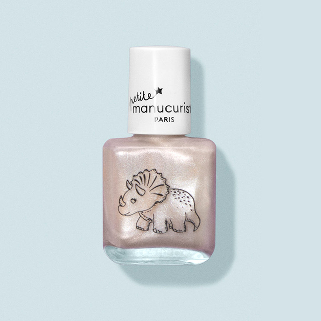 Un flacon de vernis à ongles pour enfants rose nacré à base d’eau appelé « Pénélope the Triceratops » de Manucurist, avec un bouchon blanc et un adorable motif de tricératops sur le devant, présenté sur un fond bleu clair.