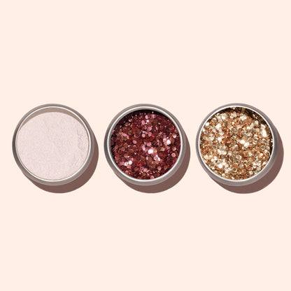 Trois petits contenants ronds ouverts renferment des poudres libres — un scintillement blanc, des paillettes biodégradables Rose Gold Manucurist et des paillettes dorées pour le nail art — disposés côte à côte sur un fond beige clair.