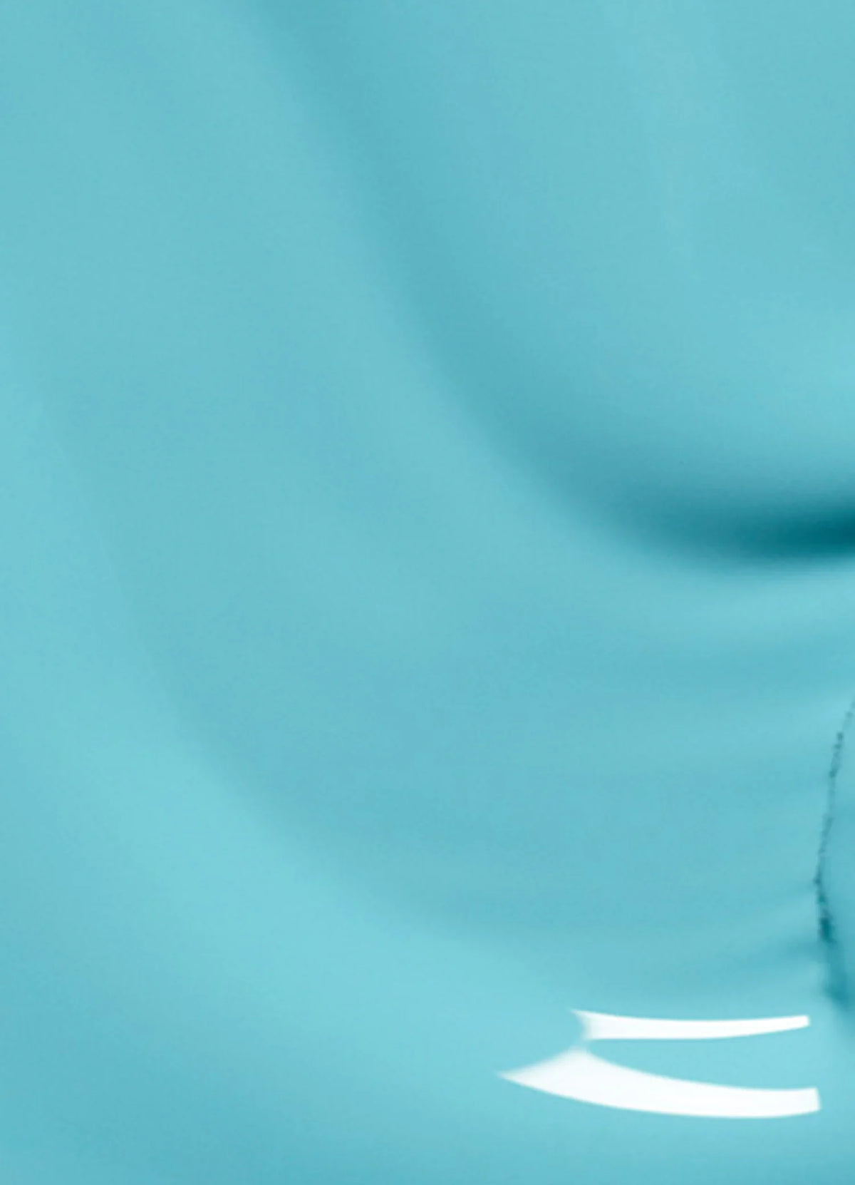 A close-up image of a smooth, light blue surface with gentle curves and subtle shading, featuring a shiny reflection and a faint crack or line near the bottom right.