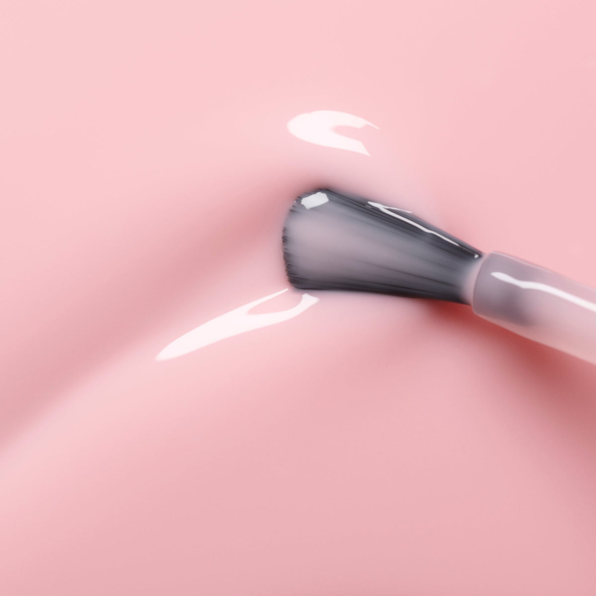 Un gros plan montre le pinceau de vernis à ongles Manucurist Hortencia appliquant un vernis rose transparent sur une surface lisse, révélant un doux reflet et de la brillance.