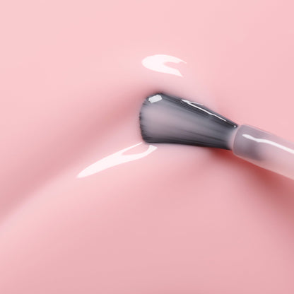 Un gros plan montre le pinceau de vernis à ongles Manucurist Hortencia appliquant un vernis rose transparent sur une surface lisse, révélant un doux reflet et de la brillance.