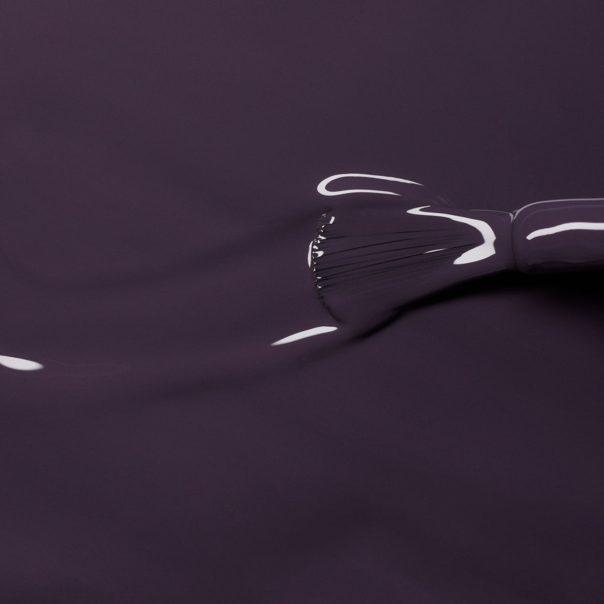 Gros plan sur le pinceau Queen of Night de Manucurist appliquant un vernis semi-permanent violet foncé brillant aux sous-tons gris, reflétant la lumière et renforçant la profondeur sur une surface lisse.