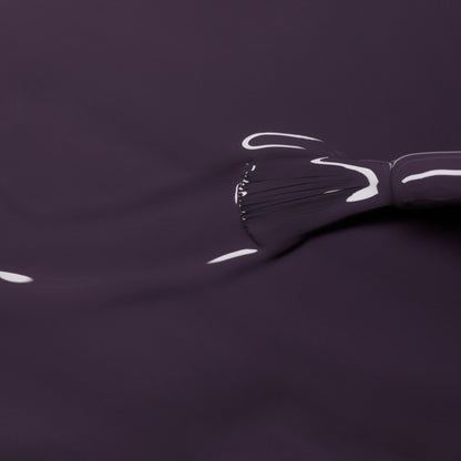 Gros plan sur le pinceau Queen of Night de Manucurist appliquant un vernis semi-permanent violet foncé brillant aux sous-tons gris, reflétant la lumière et renforçant la profondeur sur une surface lisse.