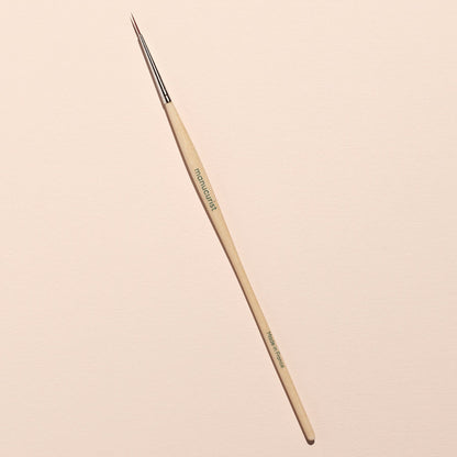 The Witchy  Wicked brush by Manucurist, featuring a wooden handle and metal ferrule, lies diagonally on a light beige surface—ideal for detailed Halloween nail art with gel polishes or adding biodegradable glitter accents.