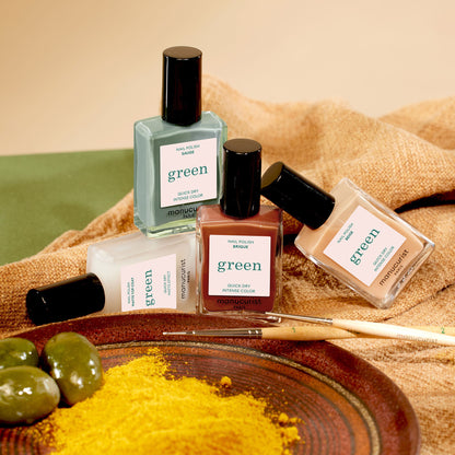 Four bottles of Manucurist’s Geometric Obsession nail polish are arranged on a brown cloth with paintbrushes, green olives, and yellow powder, creating an inspiring setup for modern nail art.