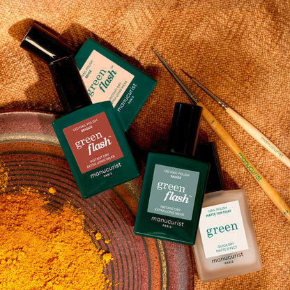 Four bottles of Manucurist Geometric Obsession nail polish in green and cream shades from the Autumn 2023 collection are displayed on a textured brown surface with yellow powder, two nail art brushes, and geometric nail art inspiration.