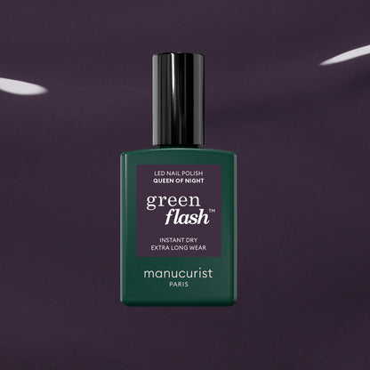 Un flacon de vernis à ongles Manucurist Queen of Night vert foncé repose sur un fond violet brillant, mettant en valeur ses sous-tons gris et son style unique.