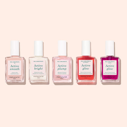 Five bottles of Manucurist Active™ nail care products stand in a row against a light beige background. Each bottle, designed for plant-based nails and topped with a white cap, features distinct label colors and names: Active™ Smooth 00, Active Bright, Active Plump, and two labeled as Active Glow.