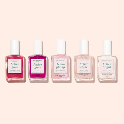 Five bottles of Manucurist nail care products stand in a row on a light pink background, with one prominently labeled “Active™ Glow Blueberry.” Each plant-based formula in the collection promises to elevate your nail care routine as a powerful nail enhancer.