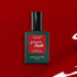 Un flacon de vernis gel Manucurist Red Velvet est posé sur un fond rouge, son flacon vert foncé et son étiquette rouge mettant en valeur la teinte glamour.